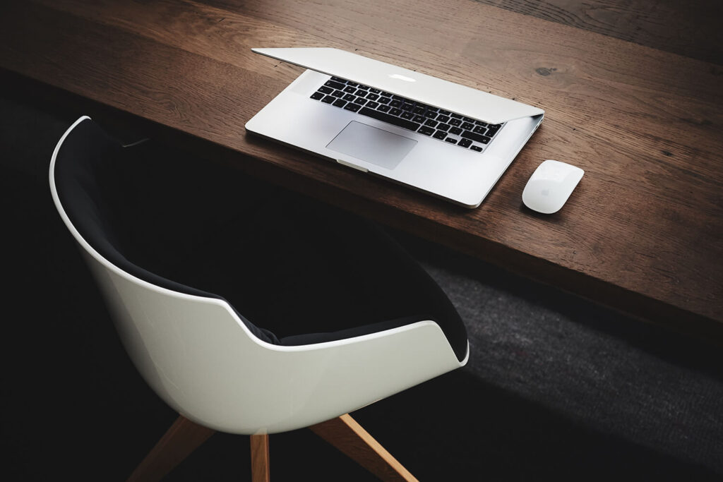 a brown desk, a white chair and a laptop with a white mouse to contact our website copywriting agency
