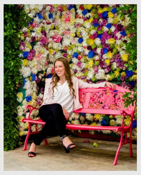 copywriting and content creation experthaley dagan sitting on a pink bench in front of a wall covered with colorful flowers