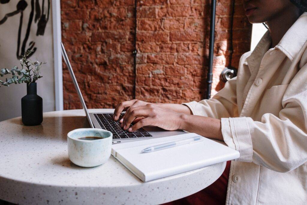 person sitting at table writing a blog on their laptop 