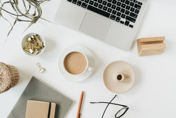 flatly image of a laptop, a cup of coffee, glasses and various items on a white office desk at our content creation agency