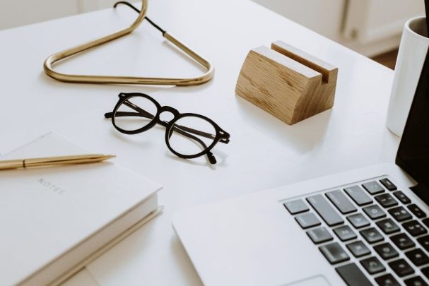 part of a laptop, glasses, a notebook and a pen on a desk for copywriting and content creation services